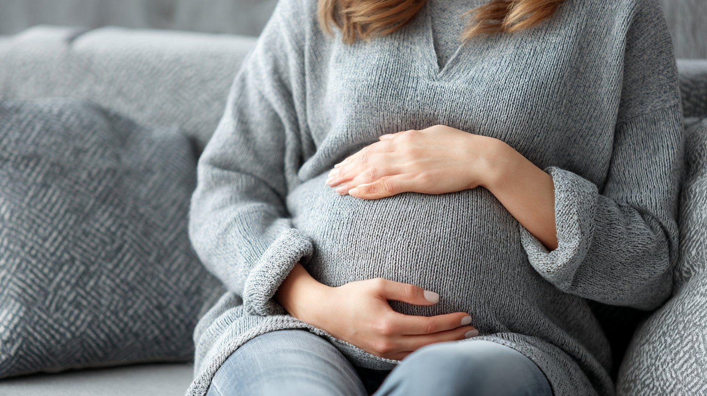 Pregnant woman sitting on couch with hands resting on stomach