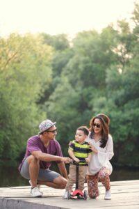 intended parents in Beverly Hills kneeling outdoors and playing with surrogate child on toy bike thanks to Made in the USA Surrogacy agency in California