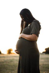 pregnant surrogacy mother in Irvine, wearing green dress and standing outdoors in a grassy field, courtesy of Made in the USA Surrogacy agency in California