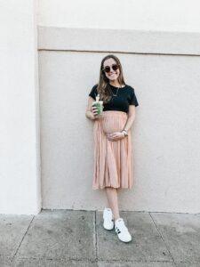 smiling pregnant surrogate mother in Foster City standing outdoors wearing beige skirt & black top, courtesy of Made in the USA Surrogacy agency in California