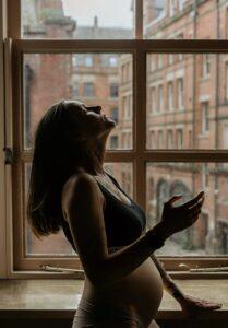 pregnant surrogate mother in Richmond, standing indoors next to window, courtesy of Made in the USA Surrogacy in California